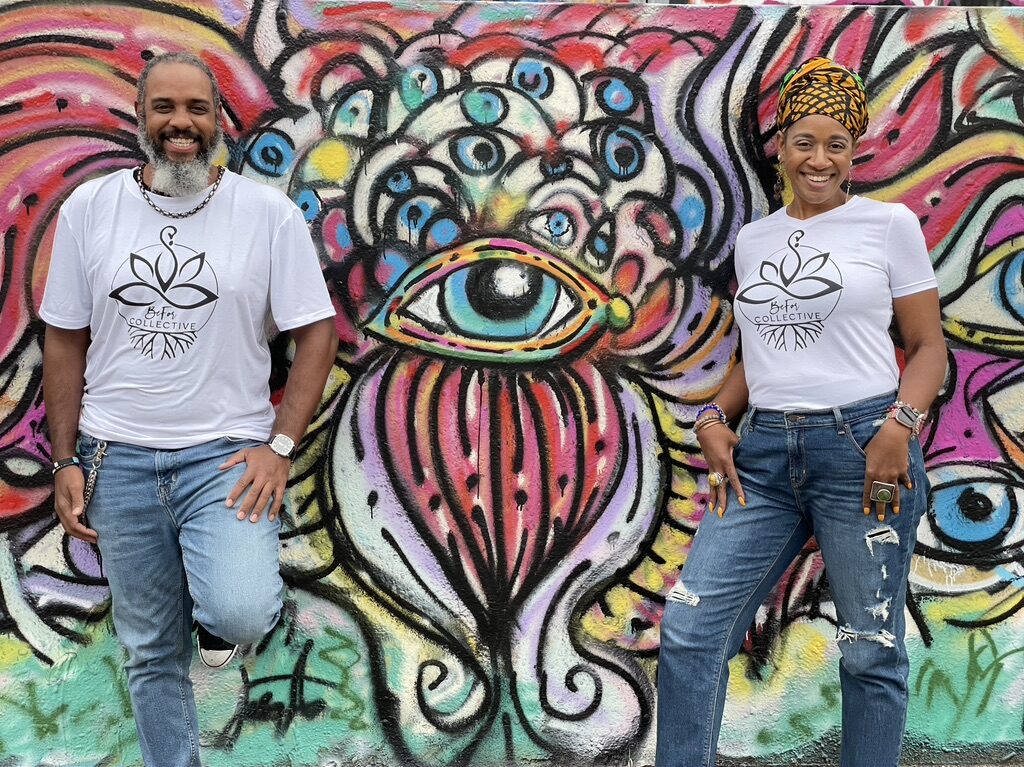 Two people posing in front of a mural with an eye on it.